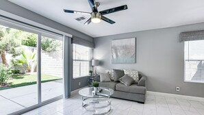Un salon spacieux avec une table basse en verre, un canapé gris et un ventilateur de plafond.