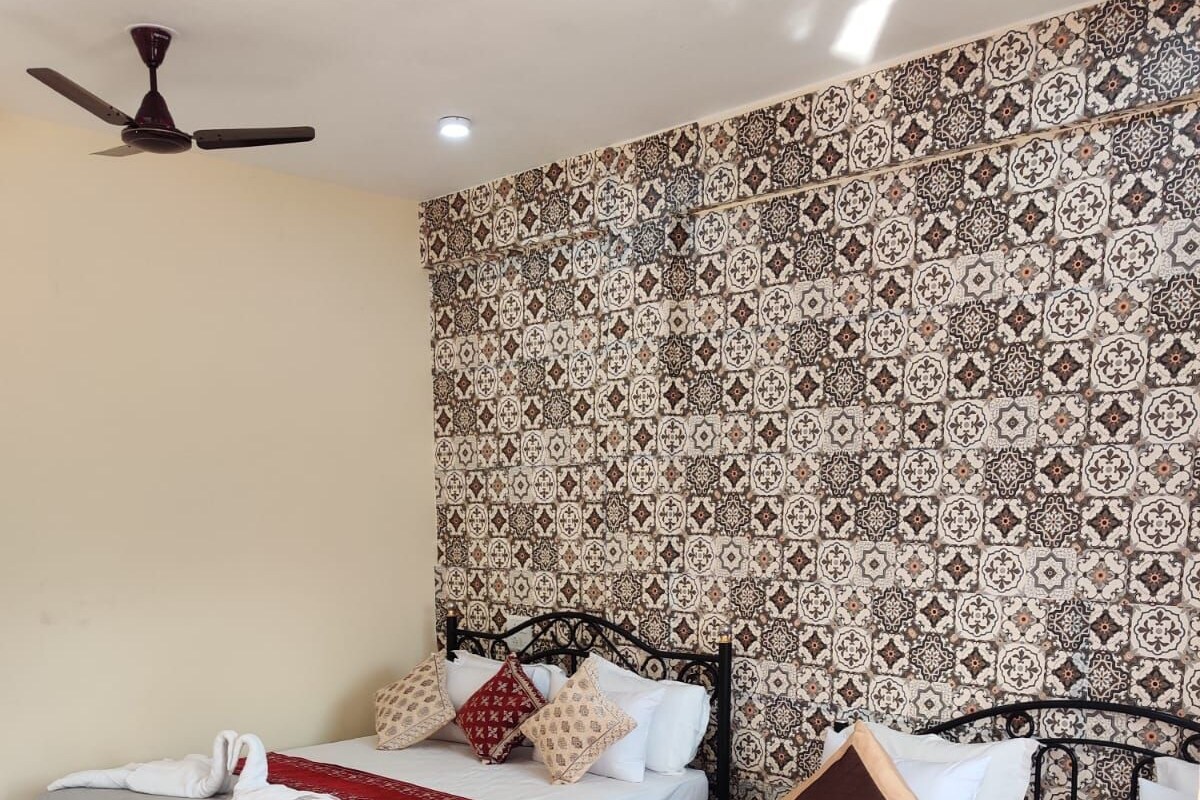 A hotel room with two beds, patterned wallpaper, a ceiling fan, and a red throw blanket on one bed.