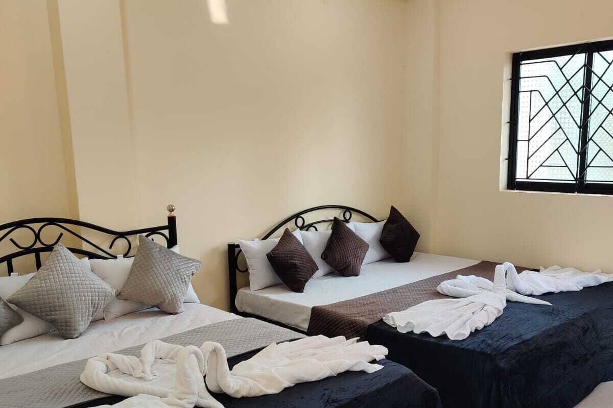 A hotel room with two beds, each with black bedspreads and white towels. There is a window with a geometric pattern and a ceiling fan.