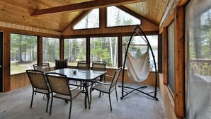 A wooden interior with a dining table and chairs, large windows, and a hanging chair.