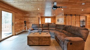 A modern log cabin interior with a large L-shaped sectional sofa, a wooden coffee table, and a ceiling fan.