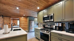 A modern kitchen with wooden ceiling, stainless steel appliances, and light green cabinets.