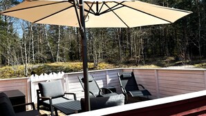 Een terras buiten met een grote parasol, enkele loungestoelen en een witte hekwerk.