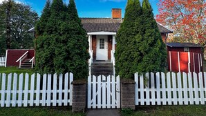 Een huis met een witte schutting, een rode tuinschuur en een rode boom met herfstbladeren.