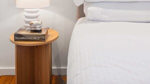 A bedroom with a bed, a bedside table with a lamp, and a window with a view of trees.