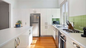 A modern kitchen with white cabinetry, a stainless steel refrigerator, a stove, and a window with a view.