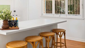 A kitchen with a white countertop, three wicker stools, a potted plant, and a window with bars.