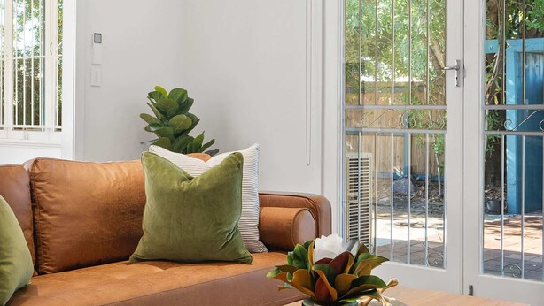 A living room with a brown leather sofa, a wooden coffee table, and a potted plant.