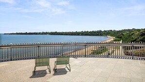 A waterfront patio with two green metal chairs and a railing overlooking a beach and water. - 5-Bed Haven with Pool Minutes From Beaches & Parks (Beaumaris)
