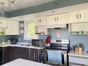 Une cuisine avec des meubles blancs, une cuisinière, un four à micro-ondes et une fenêtre.