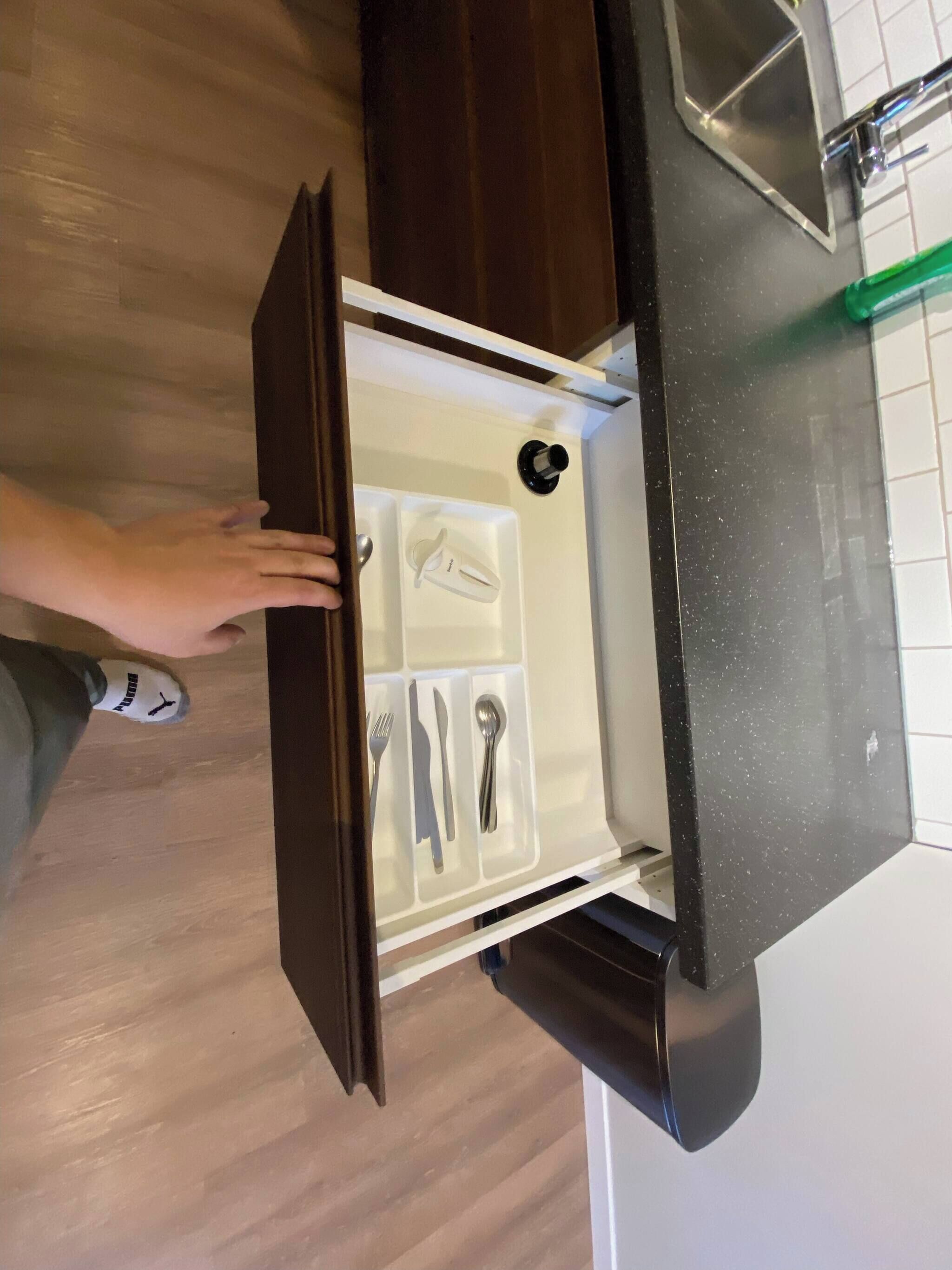 Cocina con encimera negra, pileta de acero inoxidable y un cajón con utensilios.