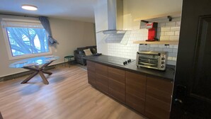 A modern kitchen with a built-in oven, a window with a view of trees, and a dining area with a glass table. - Close To Whyte University   New Renovation (Edmonton)