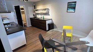 A modern kitchen with white cabinets, a black countertop, and a glass dining table with yellow chairs. - Close To Whyte University   New Renovation (Edmonton)
