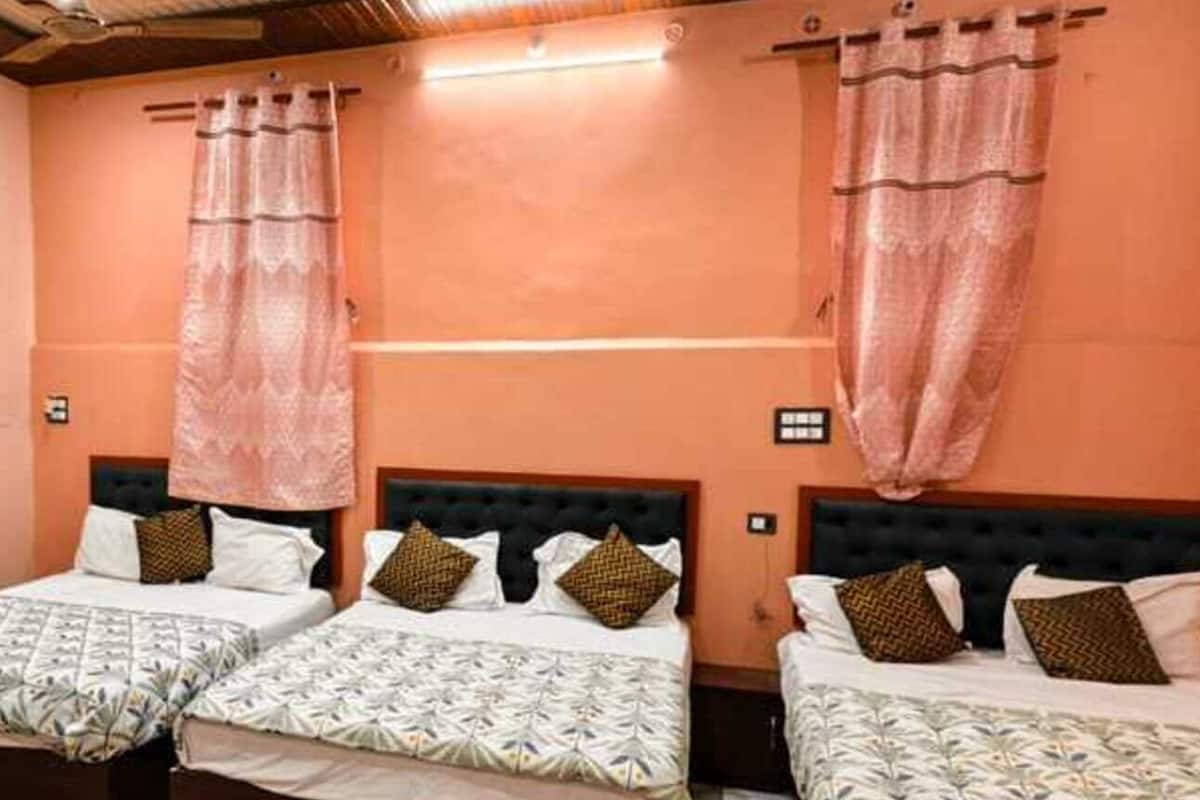 A hotel room with three beds, each with a patterned bedspread and decorative pillows.