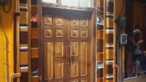 Une porte en bois surmontée d’une fenêtre, le tout intégré dans un mur jaune, avec une échelle métallique fixée sur le côté gauche.
