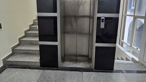 An elevator with a green exit sign, a stairwell with granite steps, and a glass door on the right. - PPH Living Royal GS Comforts Opp Mall of Asia (Bengaluru)