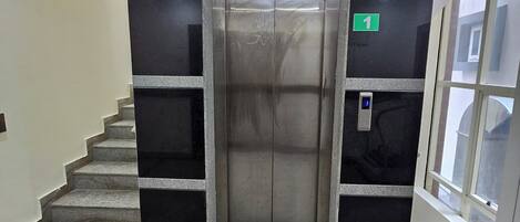 An elevator with a green exit sign, a stairwell with granite steps, and a glass door on the right.