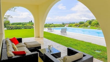 Ein überdachter Außenbereich mit Blick auf ein Schwimmbad und einen angelegten Garten.