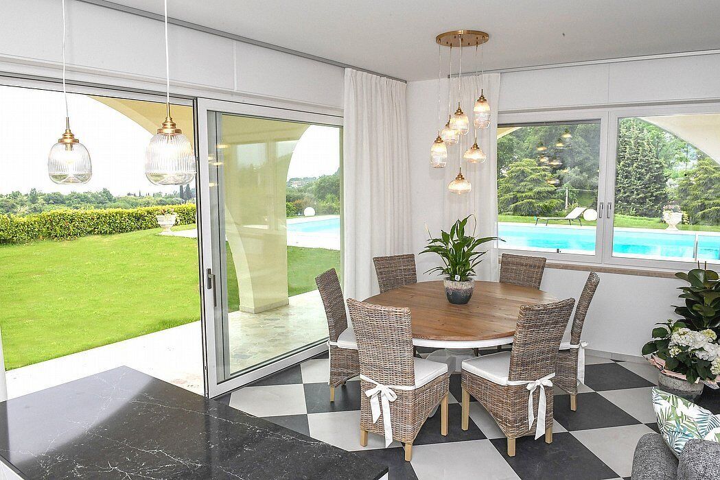 Un coin repas avec une table ronde, des chaises en osier et une vue sur une piscine et la verdure.