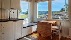 A kitchen with white cabinets, a wooden table, and a view of a rocky landscape through large windows.