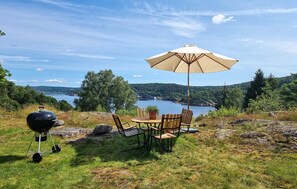 Un montaje para picnic con una parrilla, mesa, sillas y una sombrilla con vistas a un lago.
