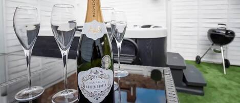 A bottle of champagne and four glasses on a table in an outdoor setting.