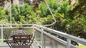 Un balcon agrémenté d’une table et de chaises, entouré d’une végétation luxuriante et doté d’une balustrade blanche.