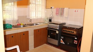 Une cuisine de taille réduite, avec des meubles de rangement en bois, un évier, une cuisinière et une fenêtre agrémentée de rideaux.