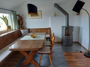 Un coin repas comprenant une table et des chaises en bois, un banc, un poêle et une fenêtre avec des rideaux.