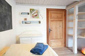 A bedroom with a bed, a wooden door, a white dresser, and a shelf with a painting. - Haevn by the Sea, Koje Room (Reußenköge)
