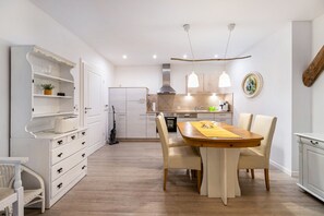 A modern kitchen with white cabinetry, a dining table with chairs, and pendant lighting. - Haevn by the Sea, Fire Room (Reußenköge)
