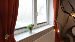 A window with curtains, a radiator, a potted plant, and a wall-mounted light fixture. - Haevn by the Sea Bird Paradise, Room Fire (Reußenköge)