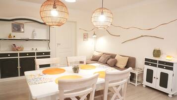 A dining area with a white table, yellow placemats, and white chairs. There is a white cabinet with black doors and a small side table with a lamp.