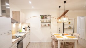 A modern kitchen with a dining area, wooden cabinets, a built-in shelf with kitchenware, and pendant lighting. - Haevn by the Sea, Luft Room (Reußenköge)