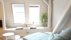 Une pièce avec un canapé bleu clair, une table en verre, un petit tabouret, une plante en pot et une fenêtre avec des stores.
