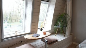 Une pièce avec une table en bois, deux fenêtres, une plante et une prise de courant.