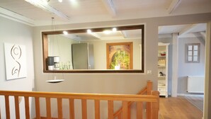 Un intérieur moderne avec un escalier en bois, un grand miroir et une vue sur une pièce comprenant une cuisine et une fenêtre.