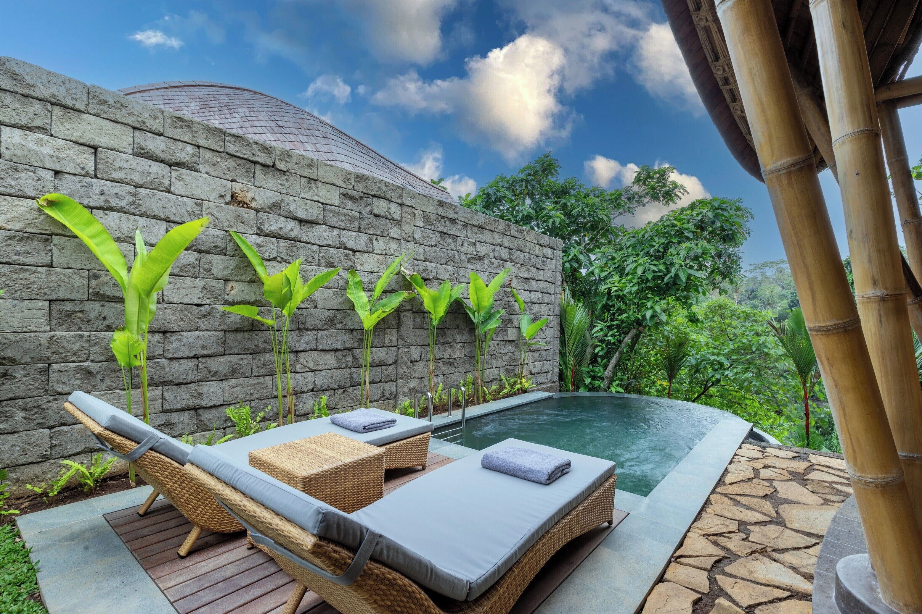 A spa area with a stone wall, a pool, and lounge chairs.