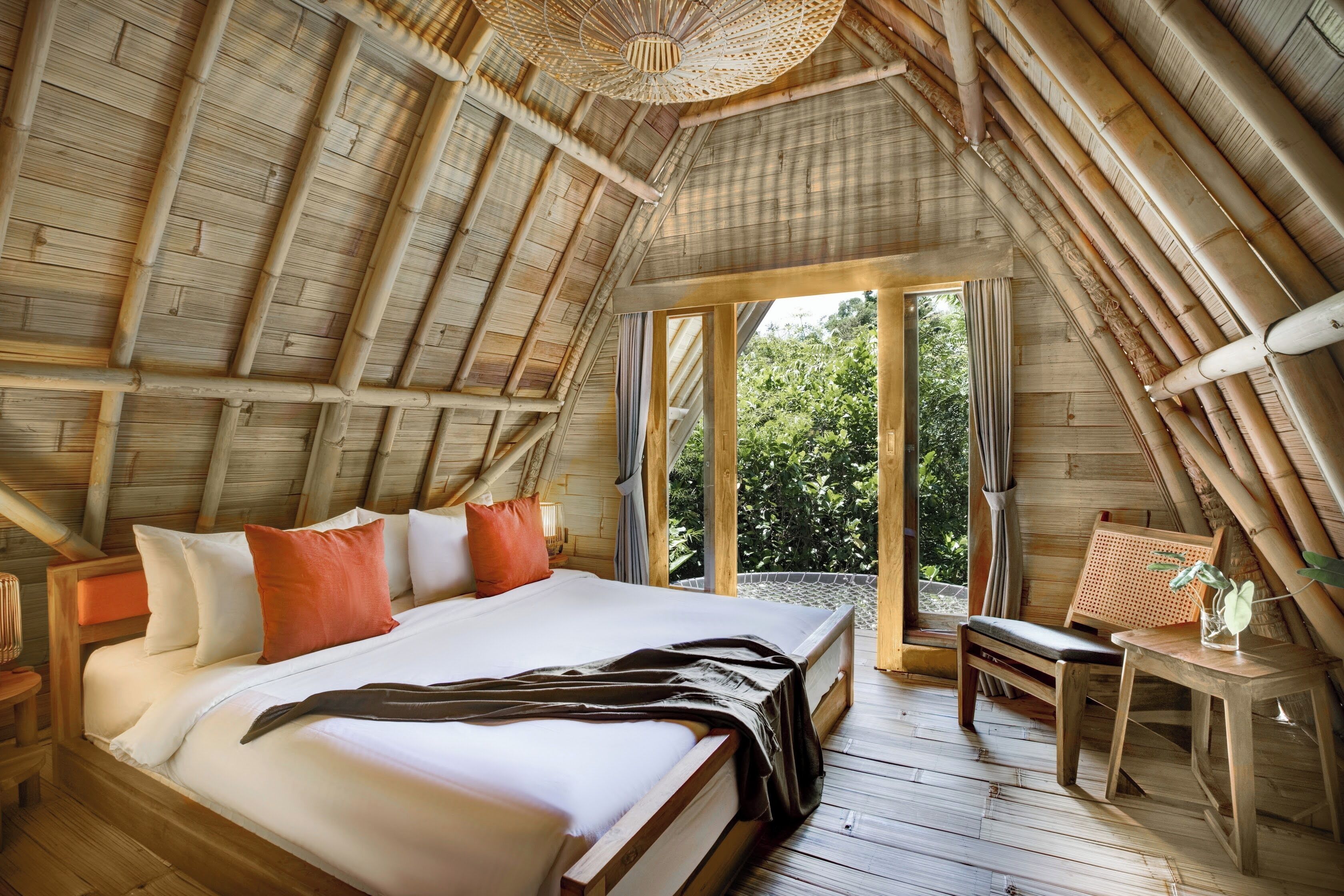 A room with a sloped ceiling, a large bed with pillows, a bench, and a small table with a plant.