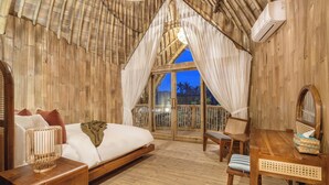 A room with a bed, a wooden table, a chair, and a large window with curtains. - Mahajiva (Abiansemal)