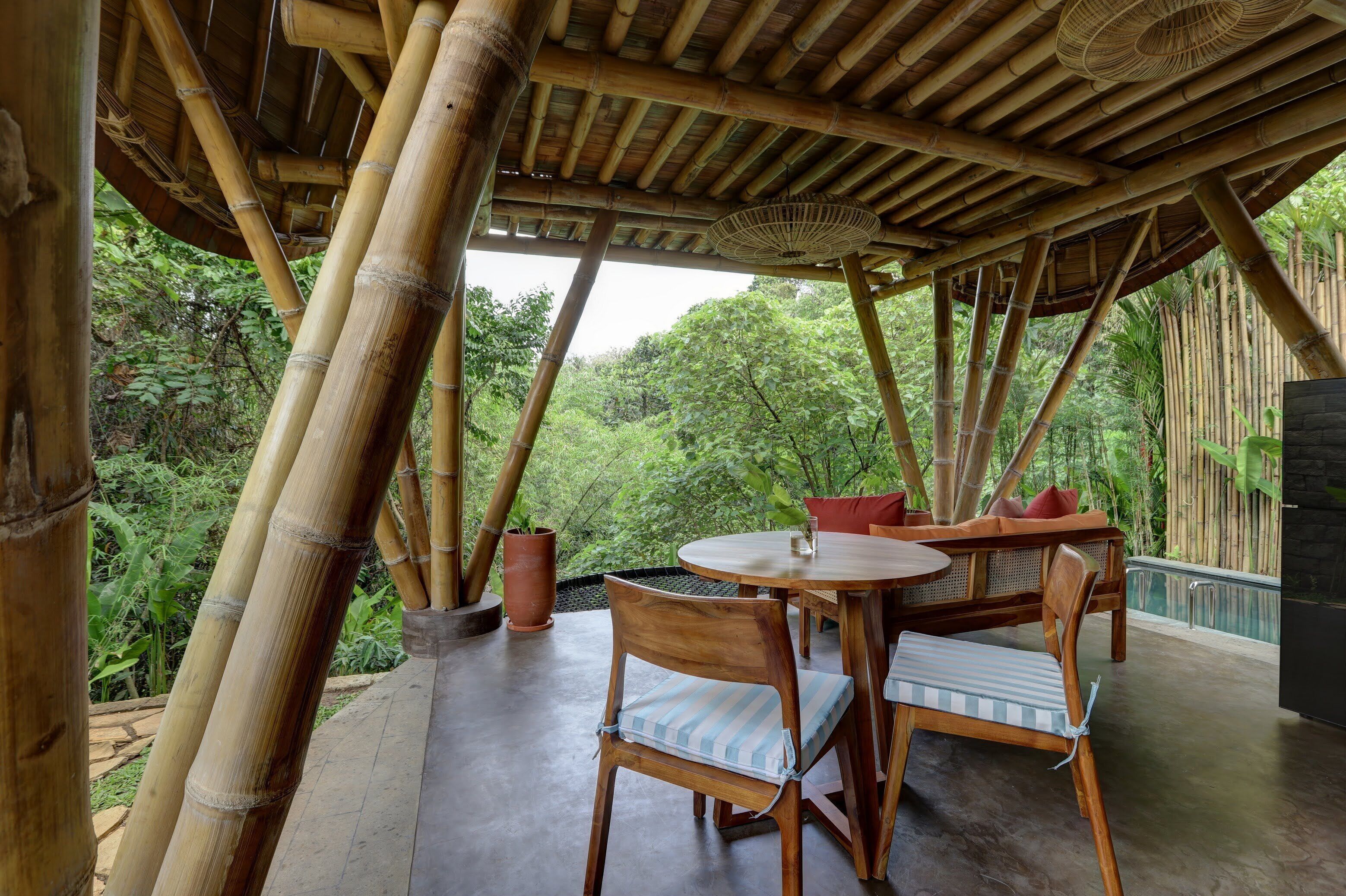 A bamboo structure with a round table and chairs, surrounded by lush greenery.