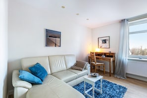 A living room with a sofa, a small table, a chair, a desk, and a window with curtains.