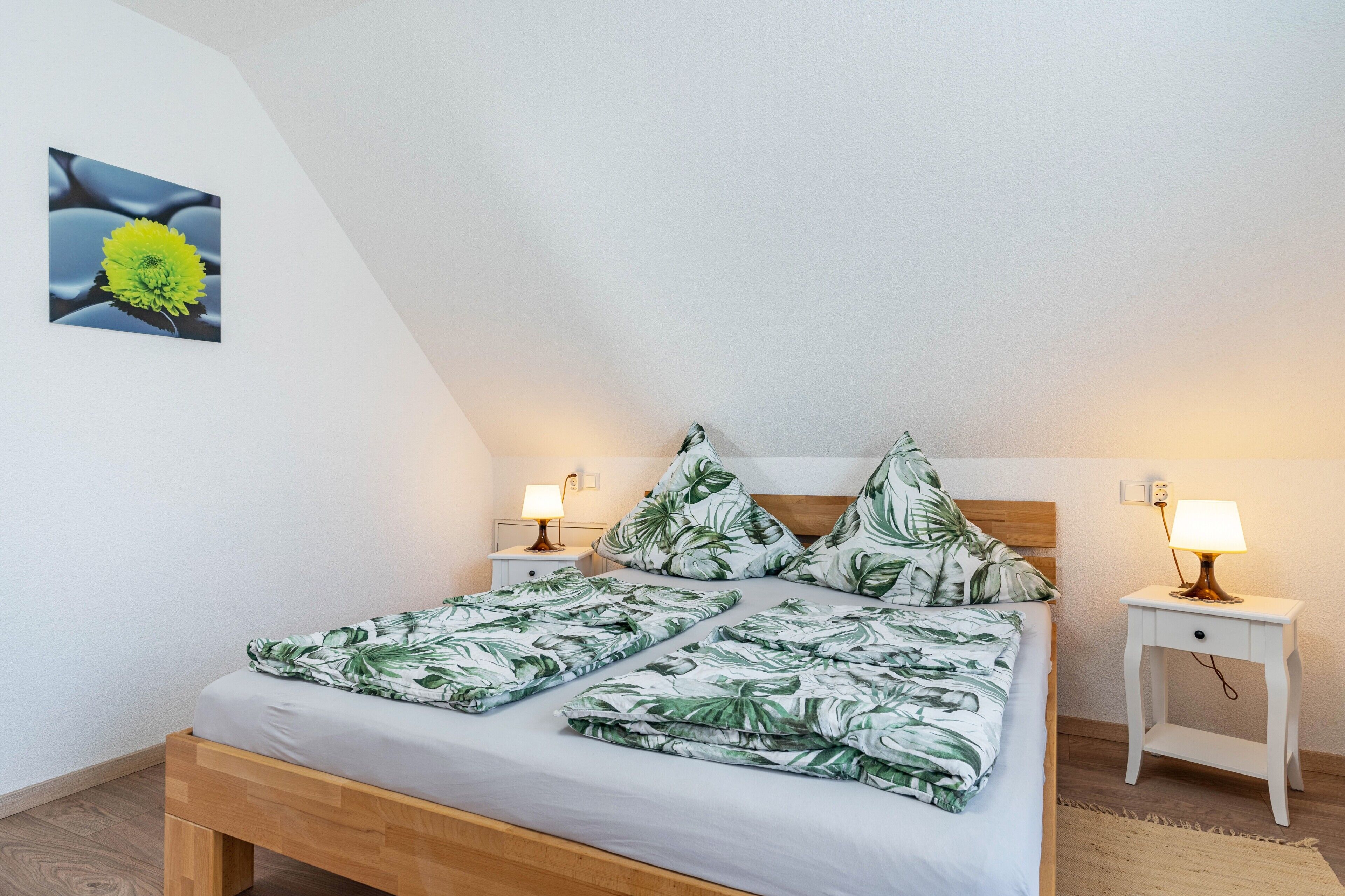 Een slaapkamer met een bed, twee nachtkastjes met lampen, een aan de muur hangend schilderij en een houten hoofdeinde.