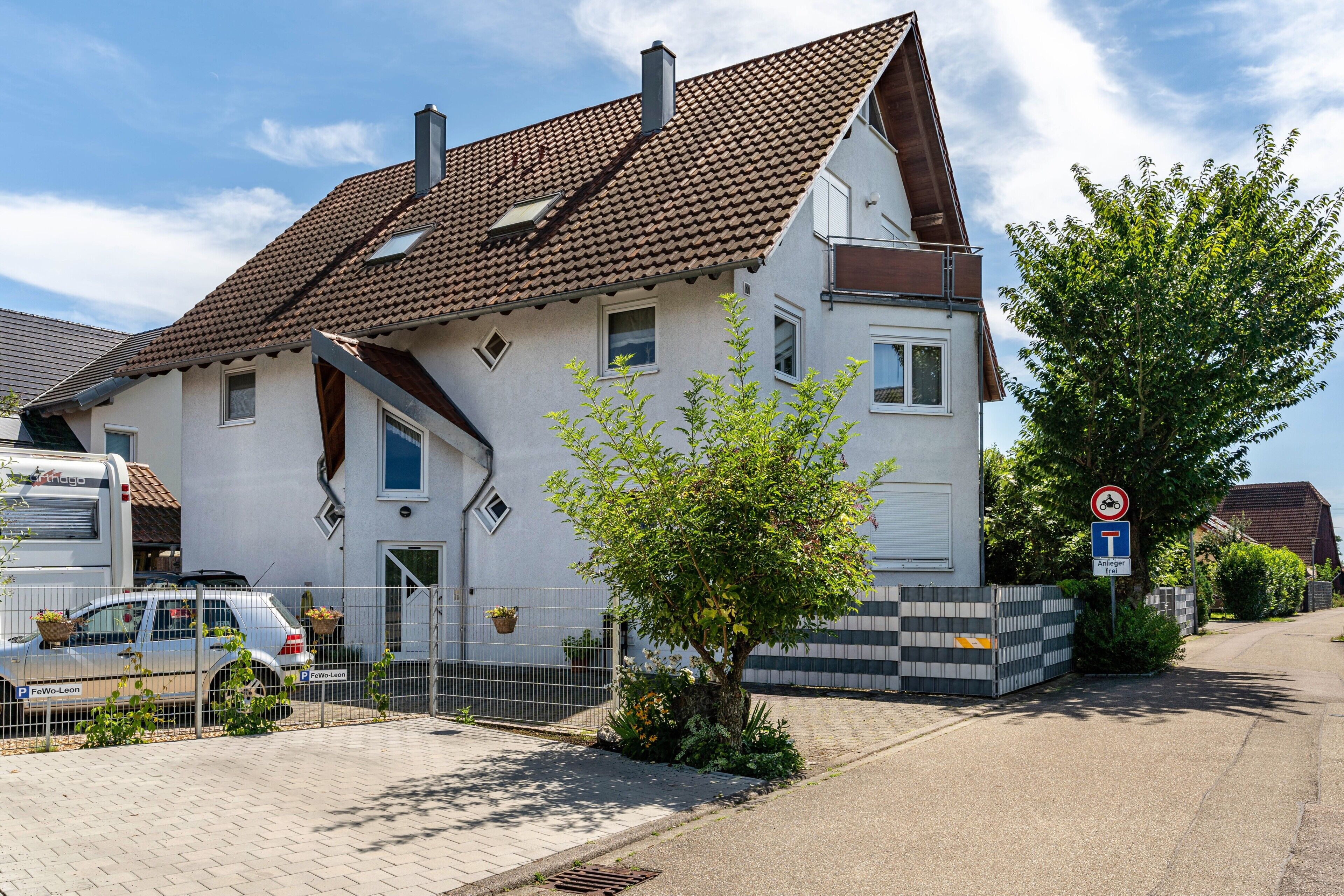 A two-story house with a tiled roof, a front door, and a small tree in the front yard.