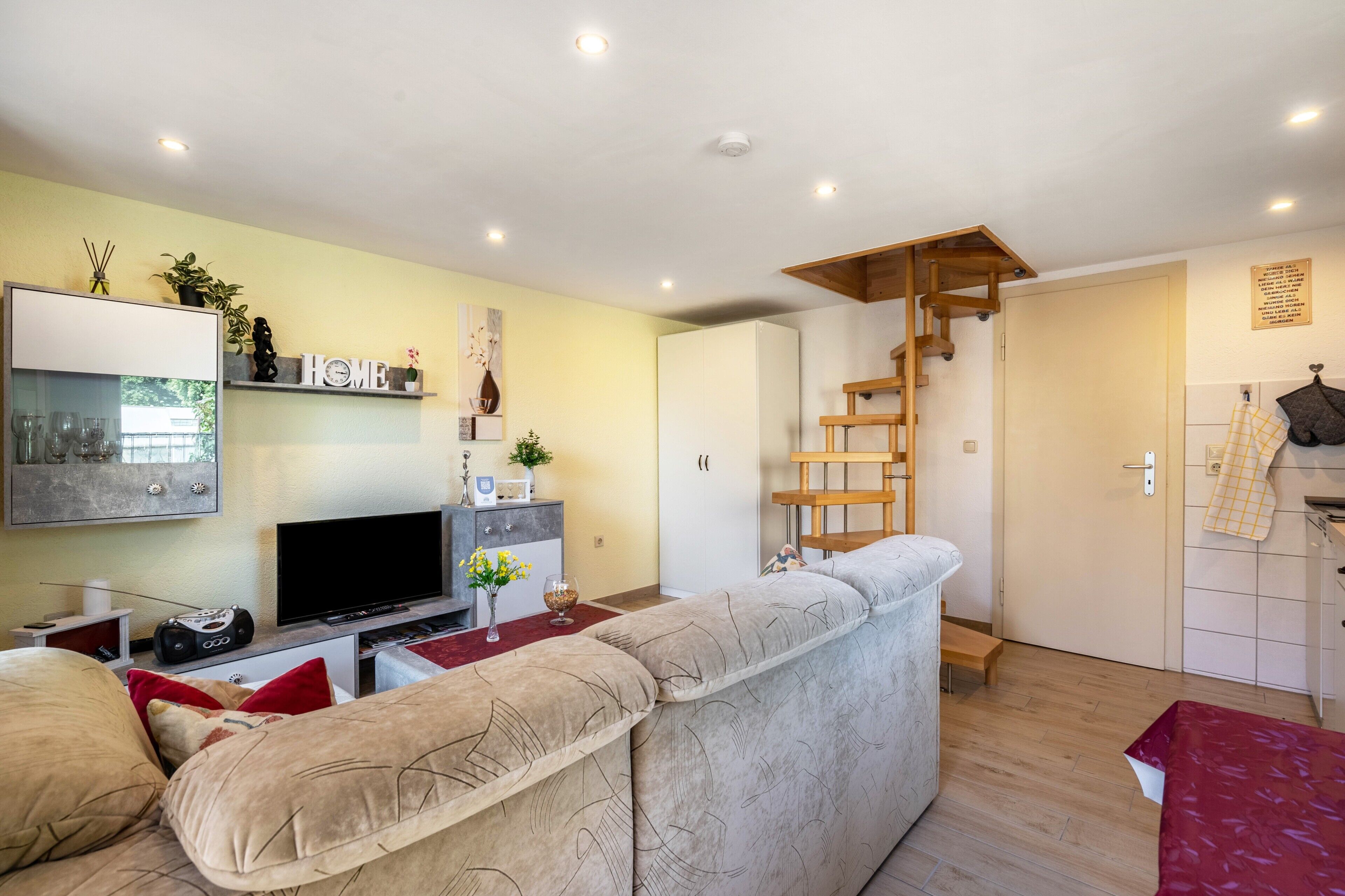 Ein Wohnzimmer mit einer Couch, einem Fernseher und einer Treppe, die in ein Schlafzimmer führt.