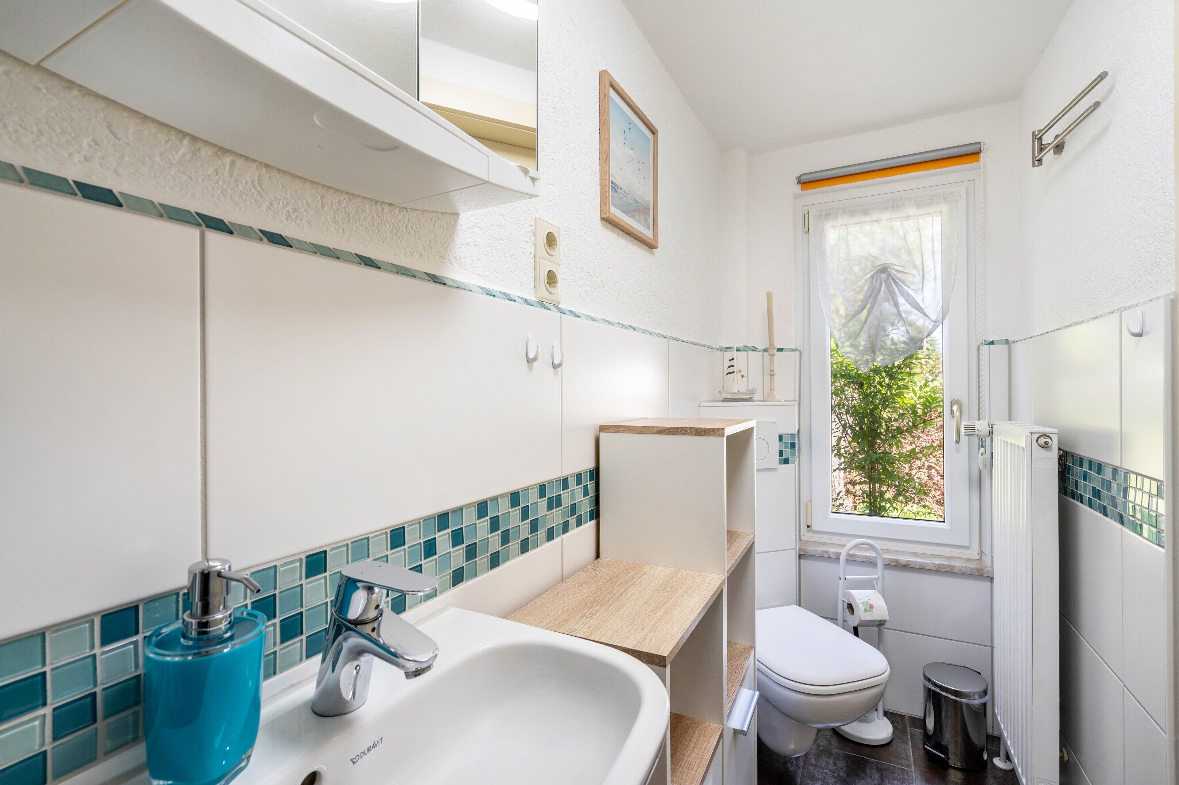 A bathroom with a white sink, blue soap dispenser, and a toilet.
