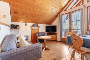 Un salon chaleureux avec un plafond en bois, une télévision, un canapé, une table et un coin repas.