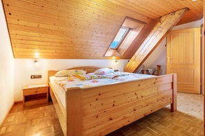 Une chambre avec un plafond en pente, un puits de lumière, un lit en bois, une table de chevet et une armoire.