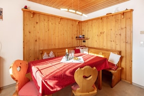 Une pièce aux murs lambrissés, avec une table dressée pour deux personnes, un banc et une étagère ornée de divers objets.