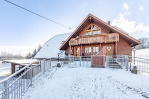 Un chalet en bois doté d’un balcon, d’un escalier menant à l’entrée et d’un sol recouvert de neige.